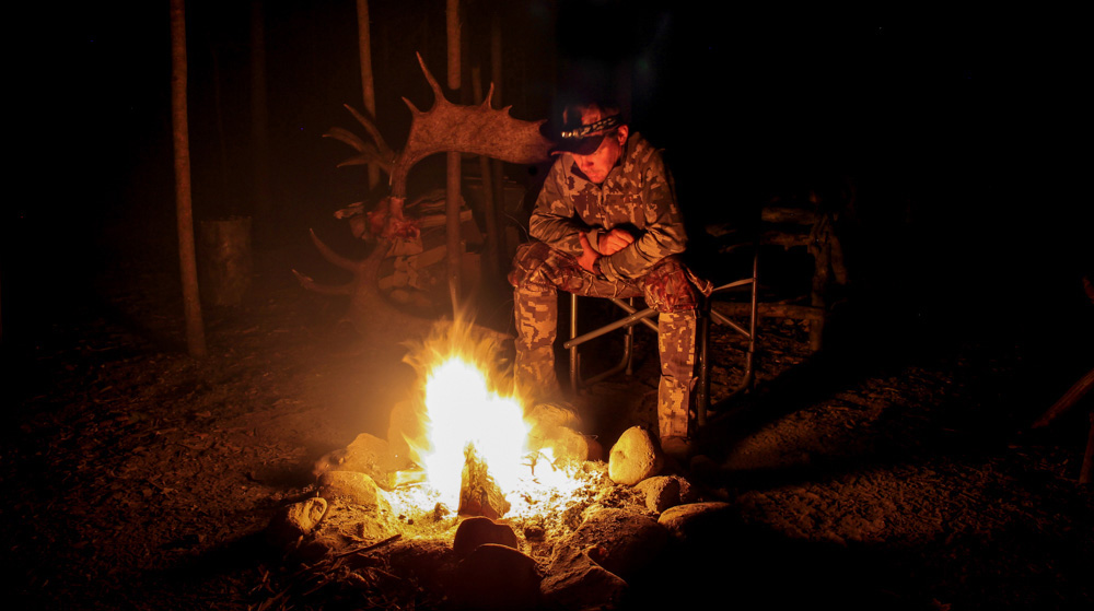 Moose hunter sitting by campfire with antlers